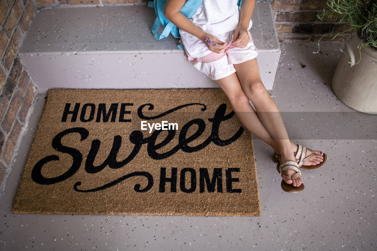 High angle view of girl sitting on retaining wall by doormat