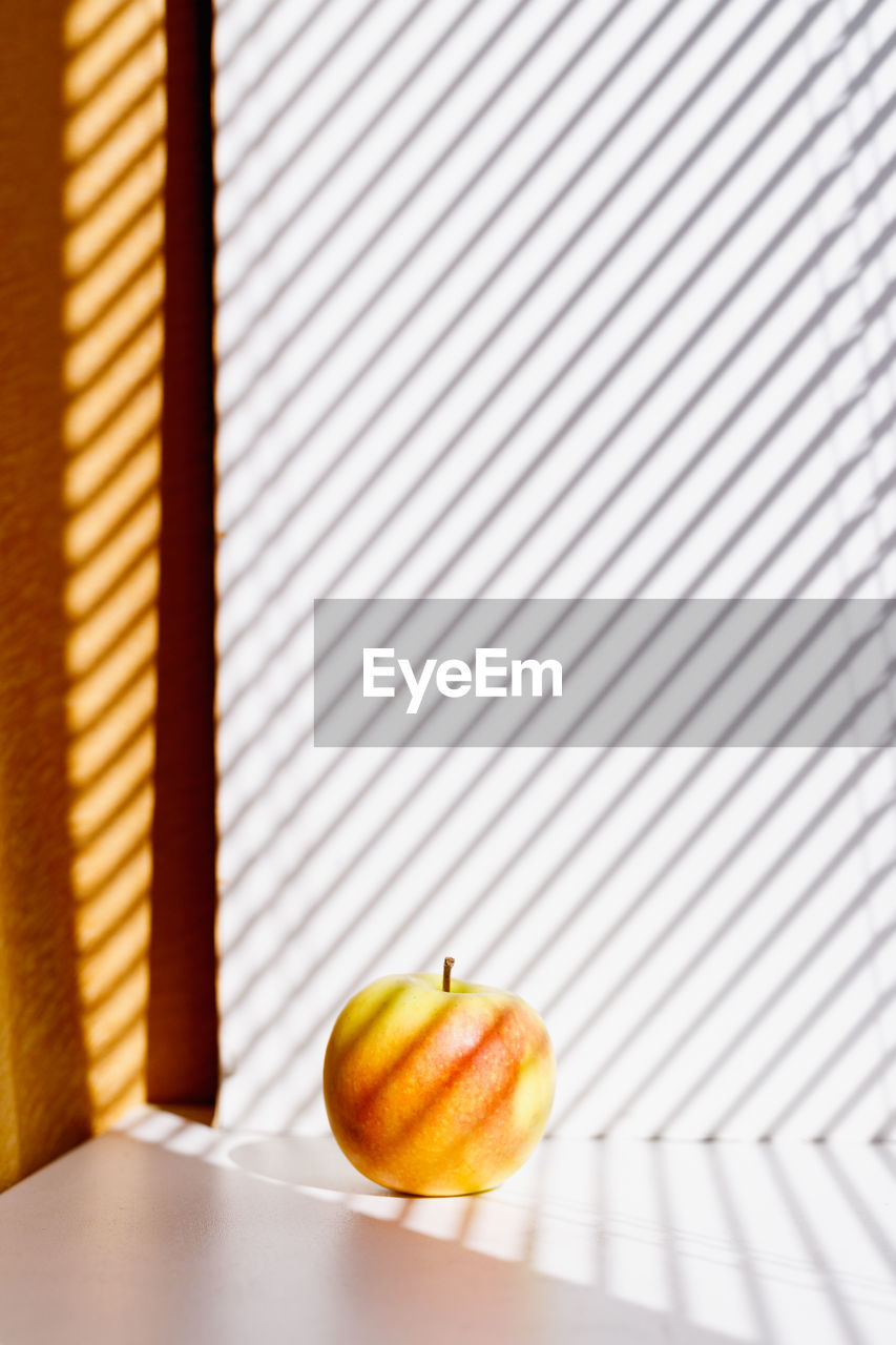 Apple on a white window sill in the sunlight and shadows of the blinds. minimalism. natural product