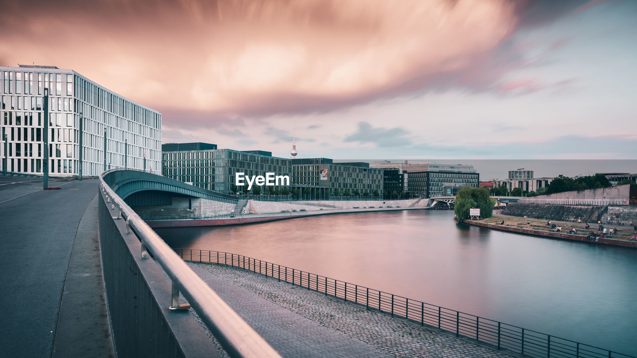 Bridge over river by buildings against cloudy sky