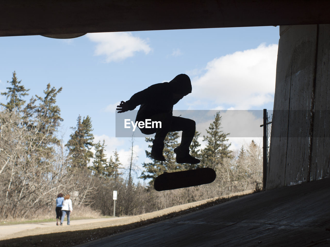 Silhouette man jumping with skateboard below bridge