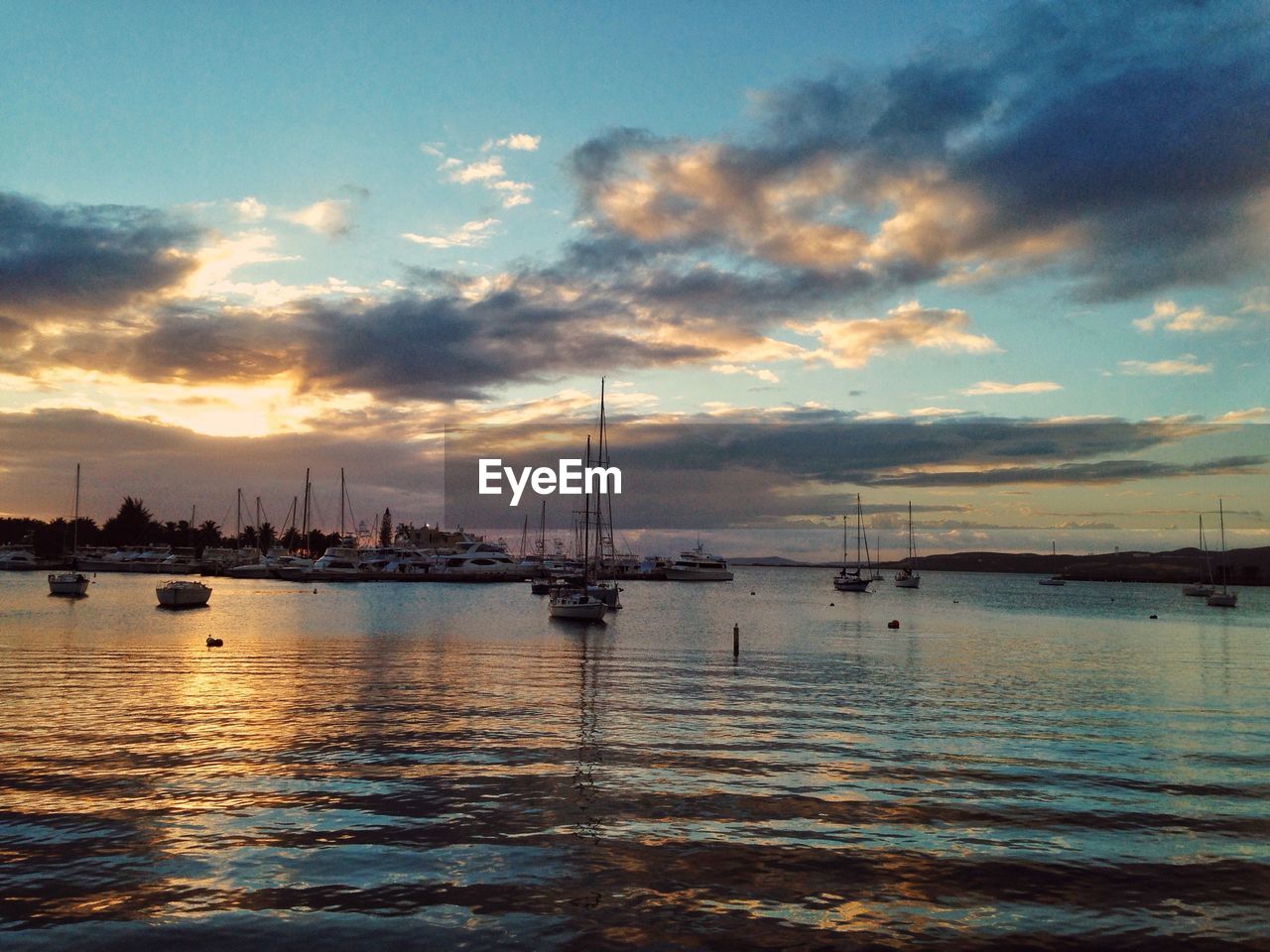 Sailboats moored on sea against sky during sunset