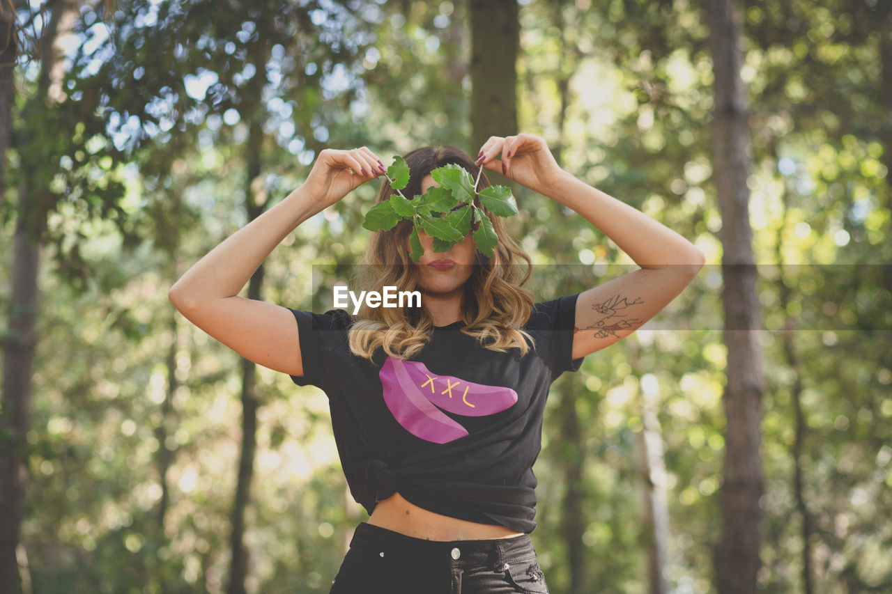 Mid adult woman covering eyes with leaves at forest