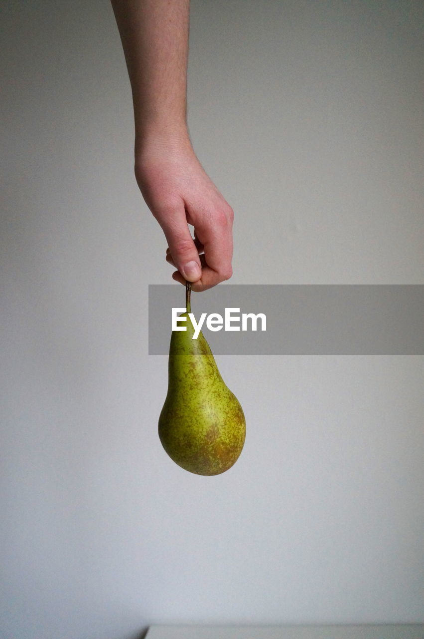 Cropped hand holding pear against wall