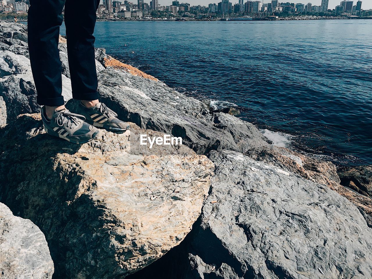 Low section of person standing on rock by sea