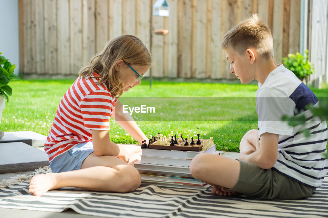 Rear view of boy playing with boys sitting outdoors