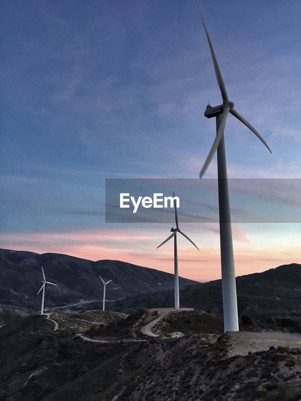 Low angle view of windmills on mountains against cloudy sky at sunset