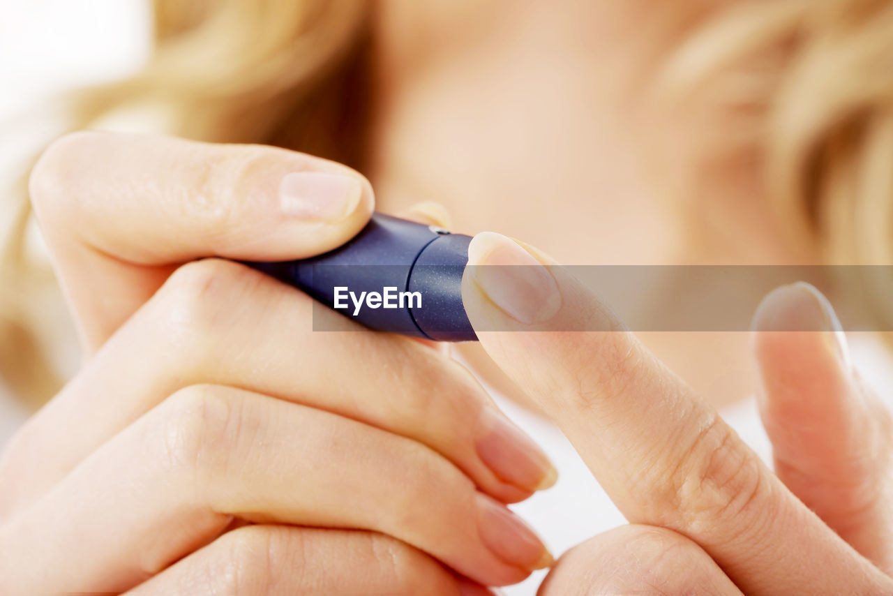 Young woman using glucose meter while examining against white background