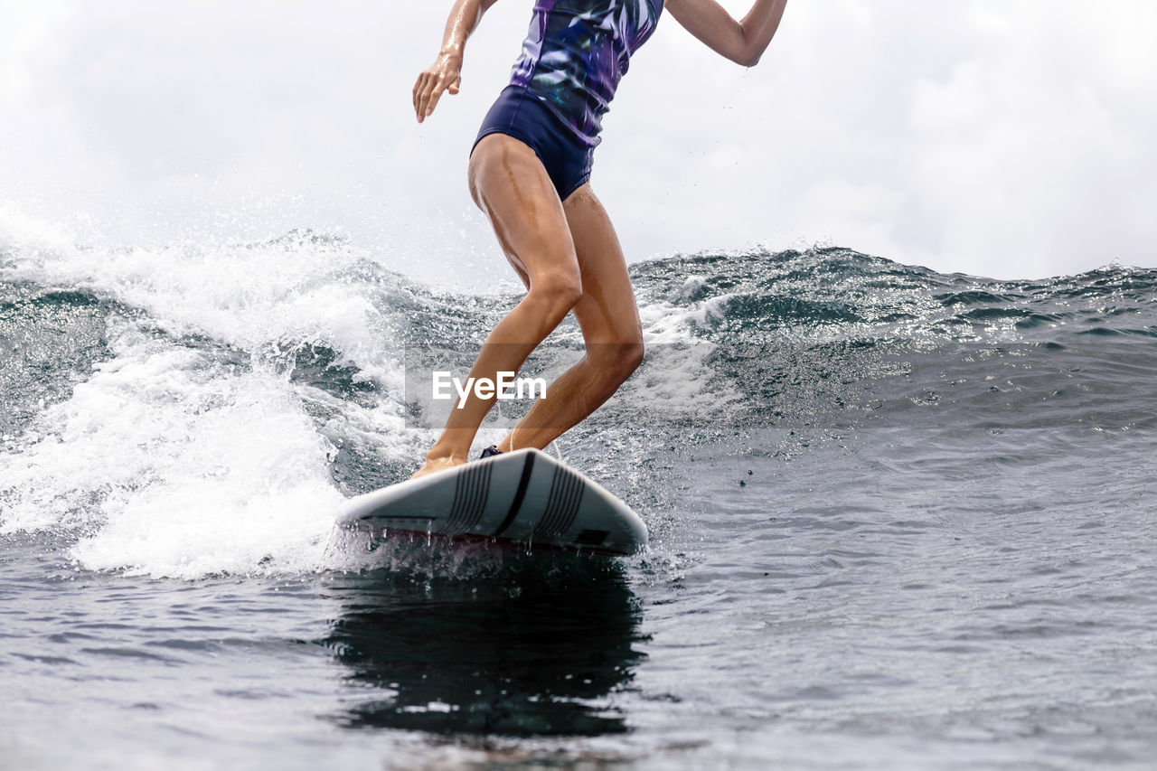 Low section of woman surfboarding in sea
