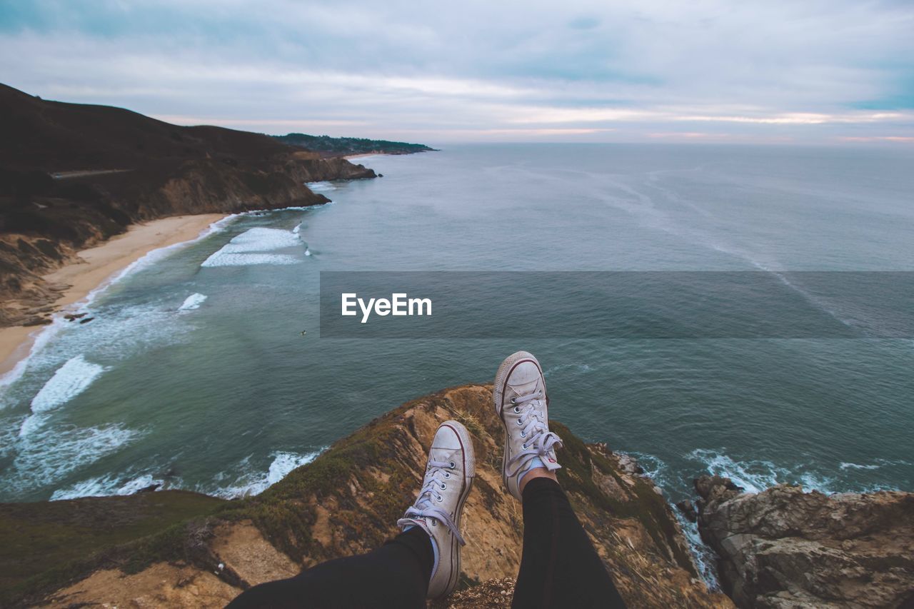 Low section of person sitting on cliff against sea