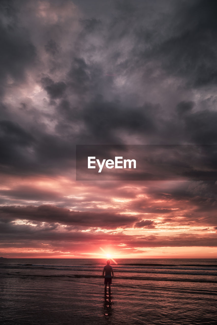 Silhouette man standing at beach against sky during sunset