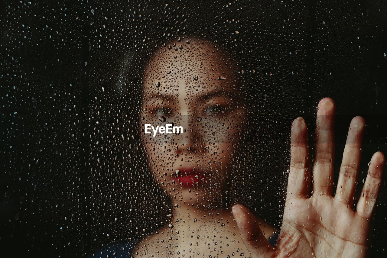 Close-up portrait of woman seen through wet window