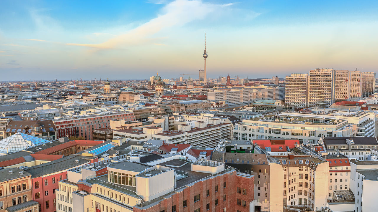 Fernsehturm amidst cityscape against sky during sunset