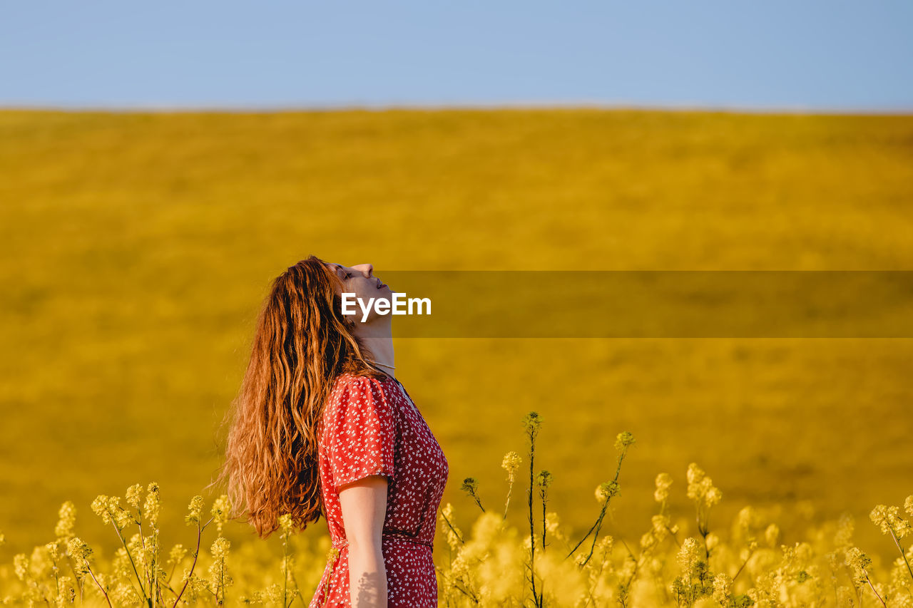 Portrait of young woman enjoying warm spring sunny weather outdoors in the blooming mustard field