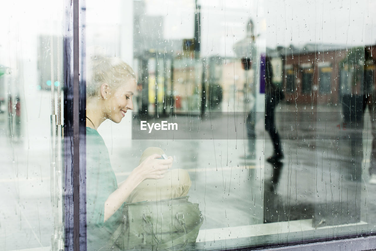 Young woman sitting on sill seen through glass at railroad station