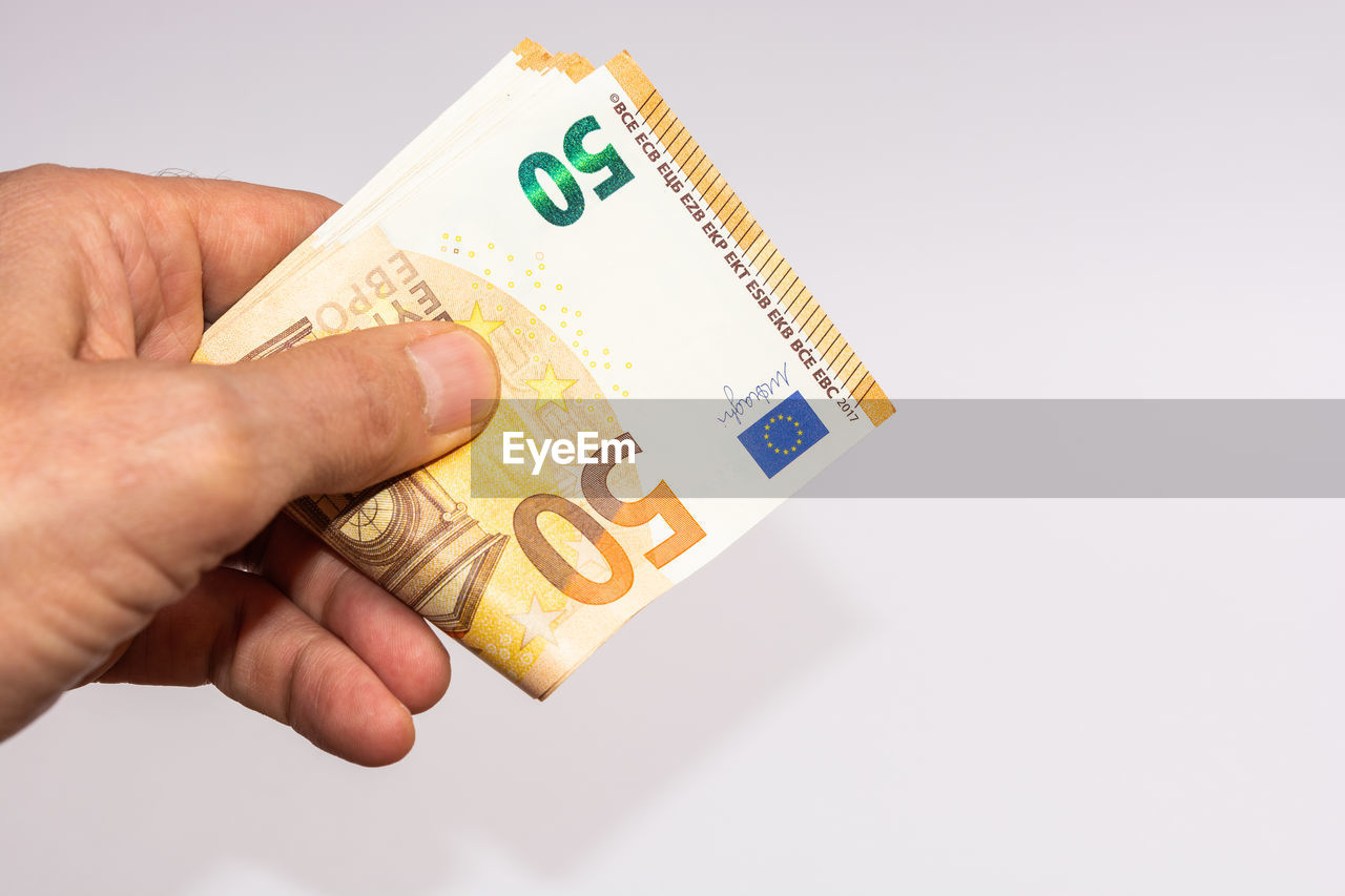 Cropped hand of man holding paper currency against white background