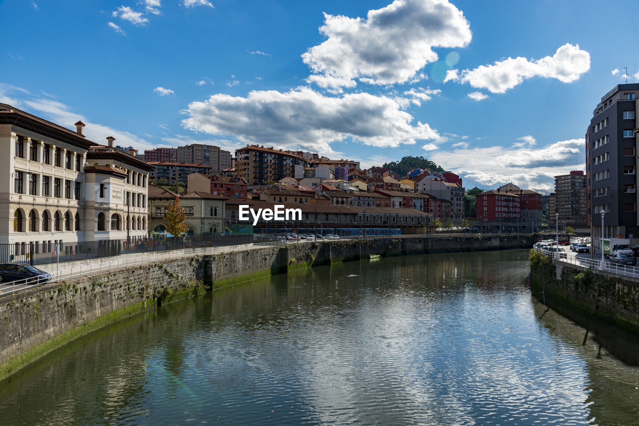 BRIDGE OVER RIVER BY BUILDINGS AGAINST SKY