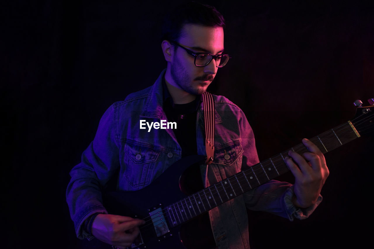 Young adult plays electric guitar under colored lights