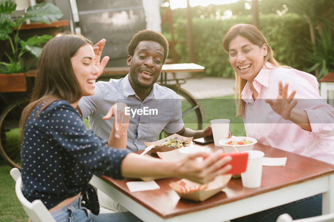 portrait of smiling friends using digital tablet while sitting on table
