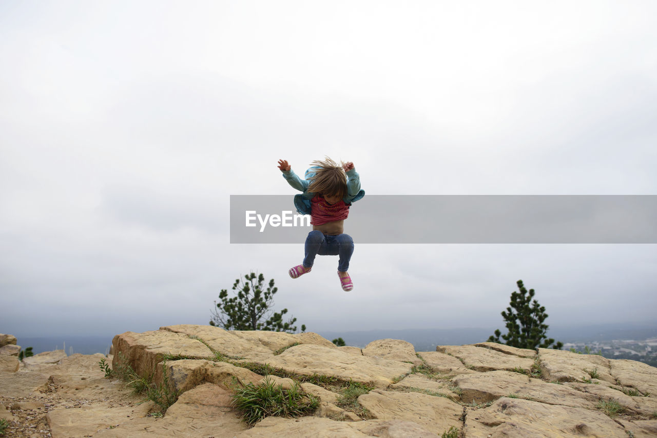 Full length of girl jumping on mountain cliff against sky at custer state park