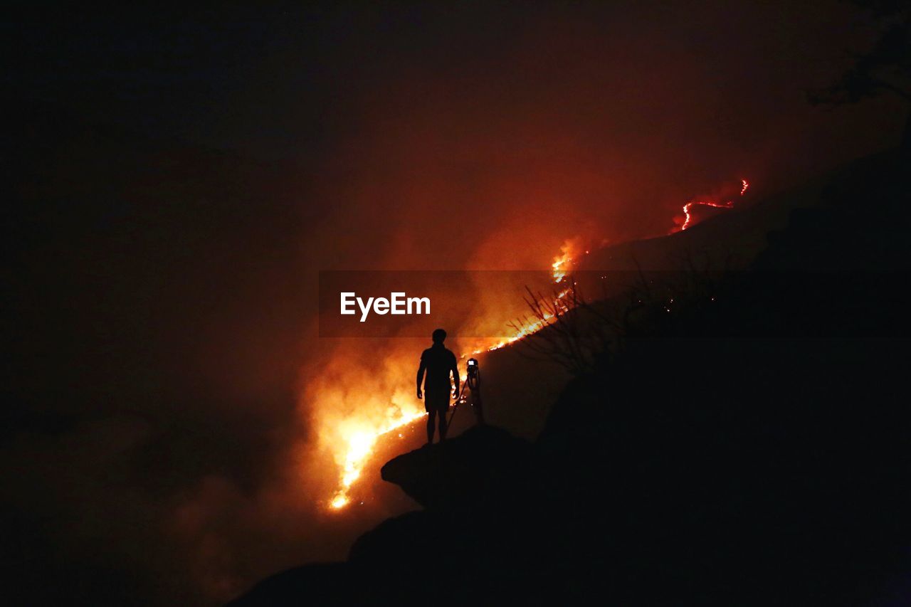 Silhouette man standing with camera against forest fire