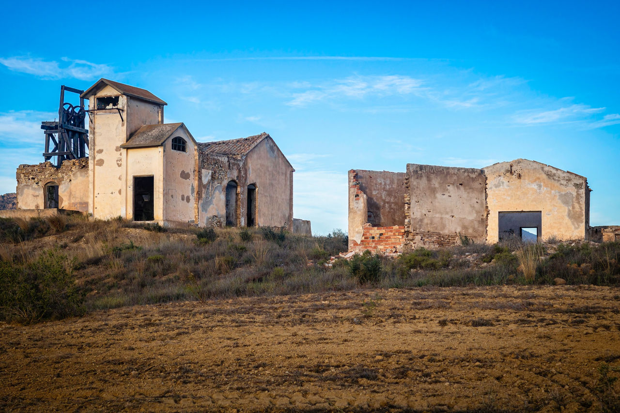 Ruins of a desolated mine with derrick and miners' buildings against sky, mazarron, spain