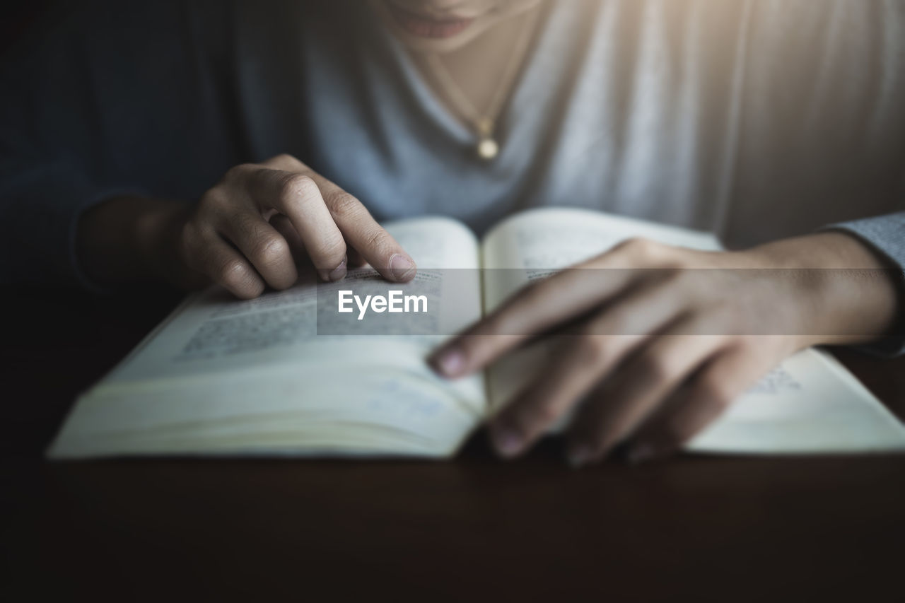 Midsection of woman reading book on table