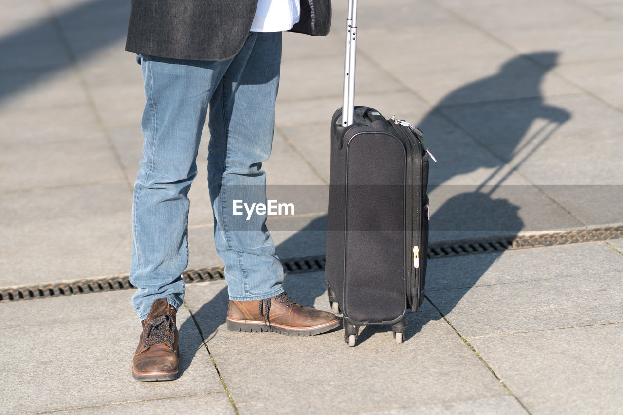 Low section of man with suitcase standing on tiled floor