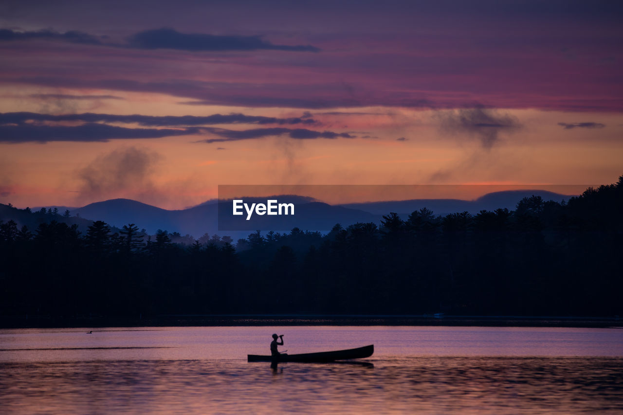 Silhouette man on boat sailing in lake against sky during sunset