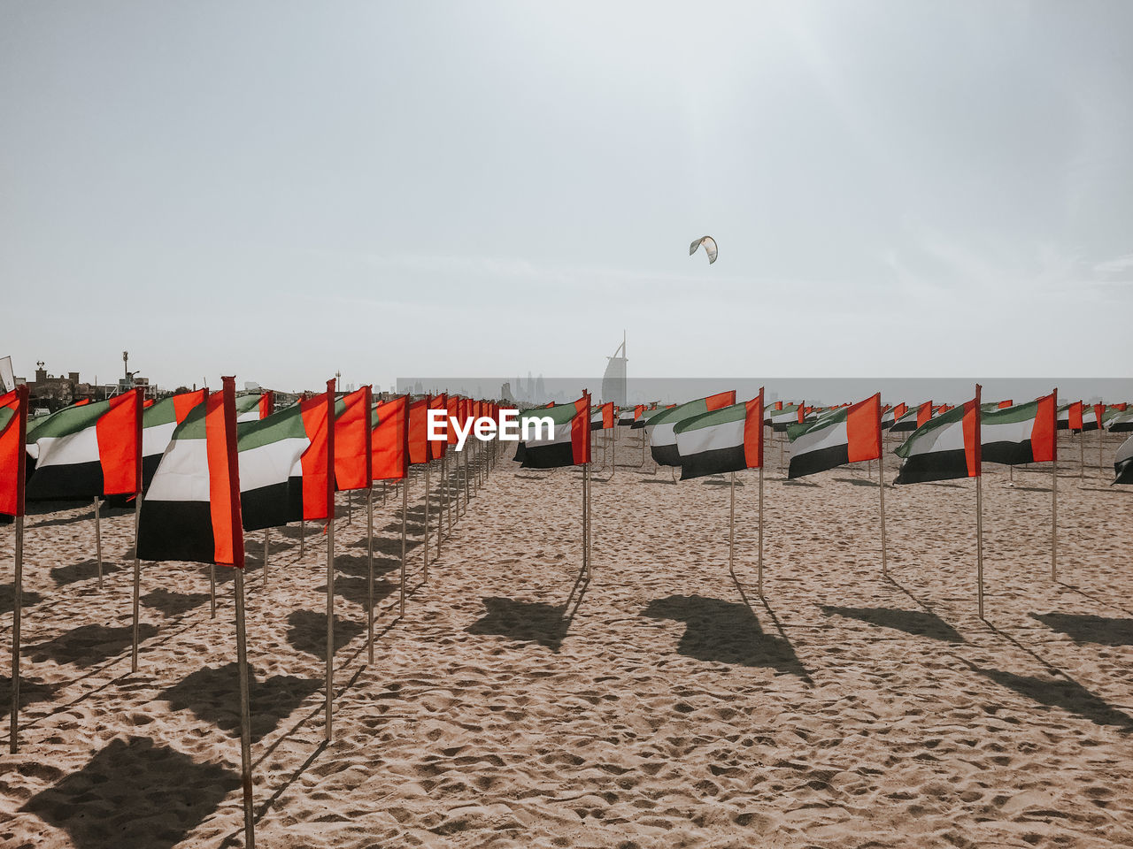 Uae flags on beach against sky, kite and burj al arab