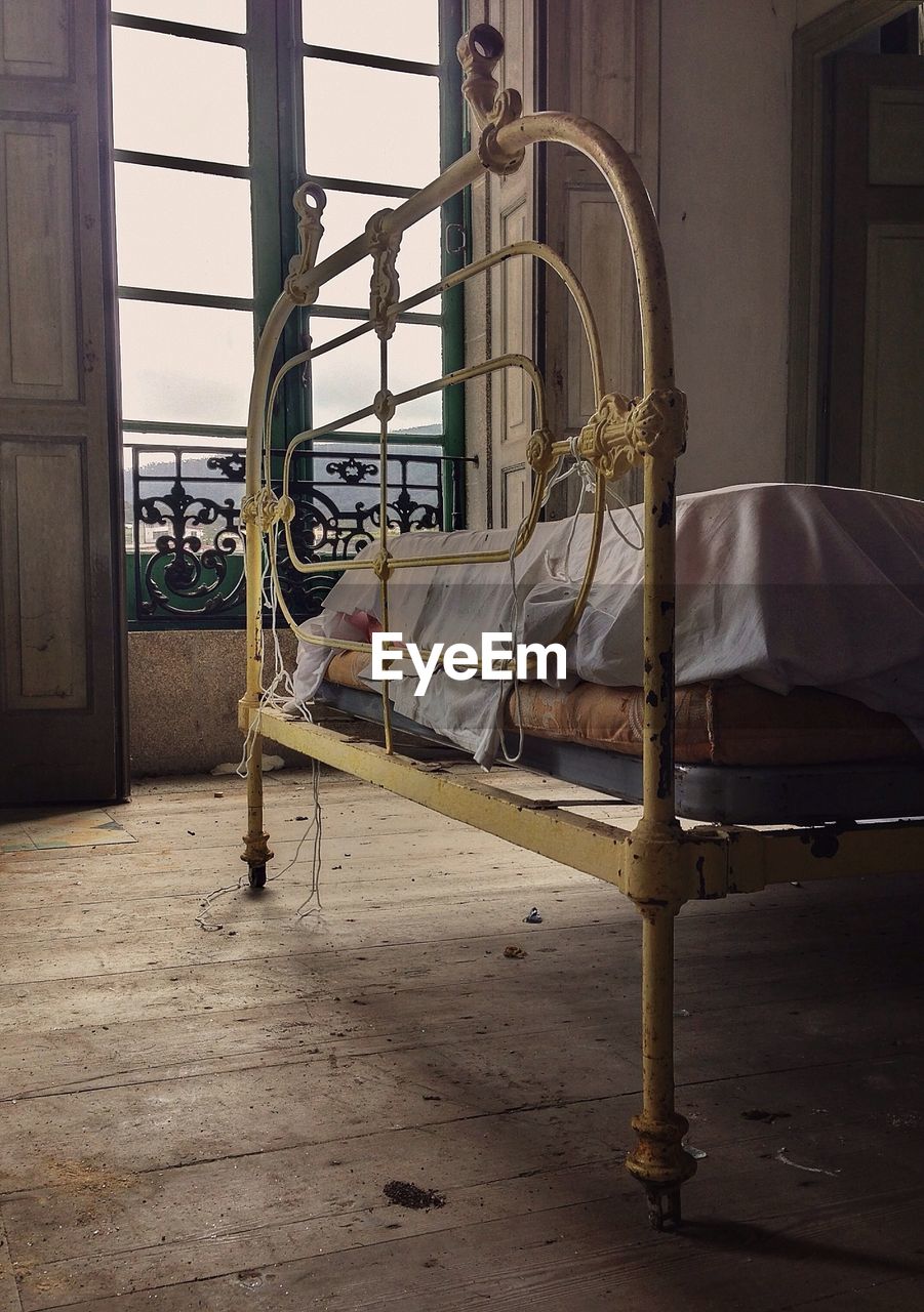 Metallic bed against window at abandoned home