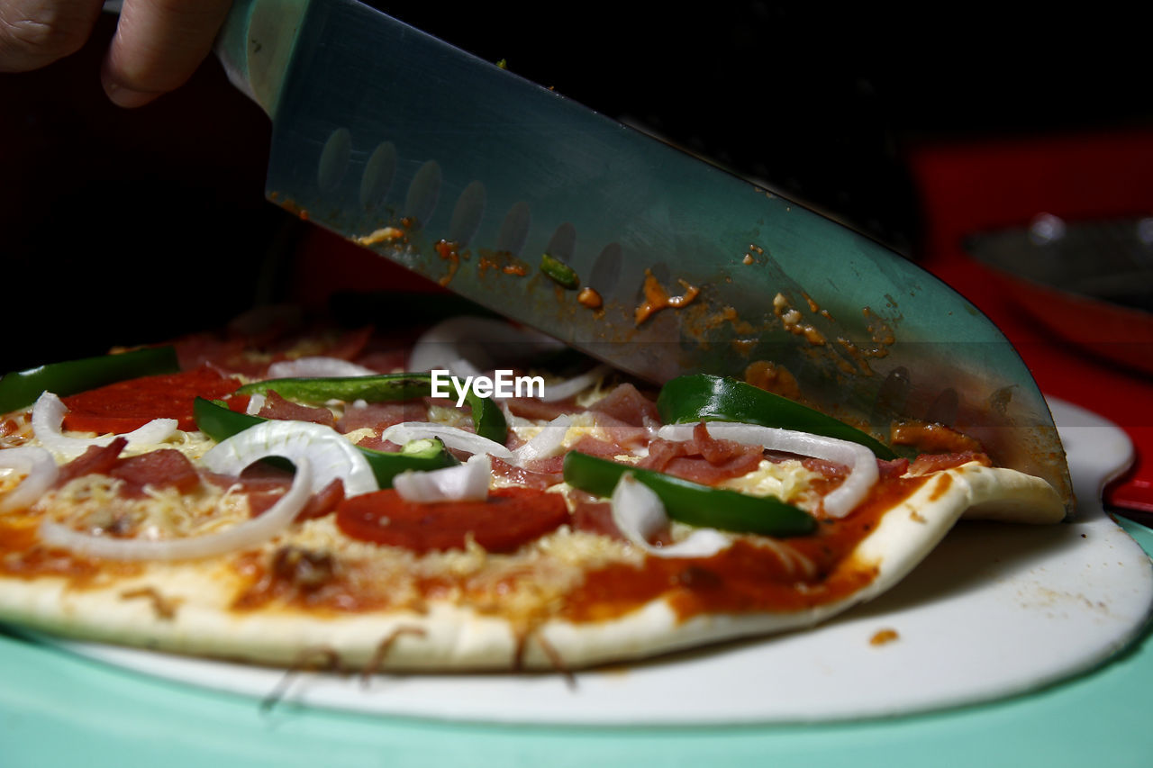 Cropped hand of person cutting pizza on table