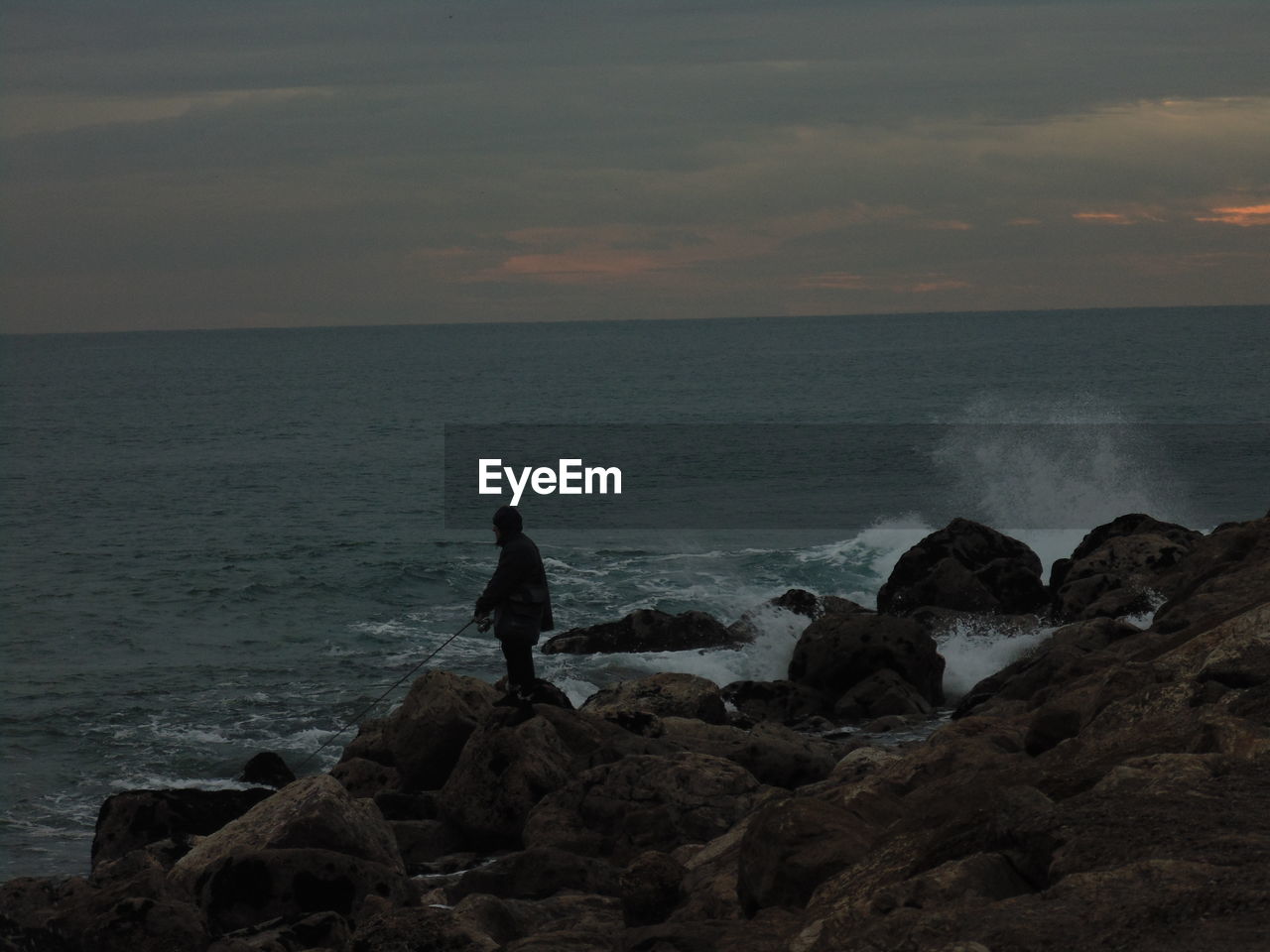 Man fishing in sea during sunset