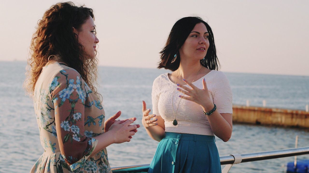Female friends talking while standing on boat deck against sea