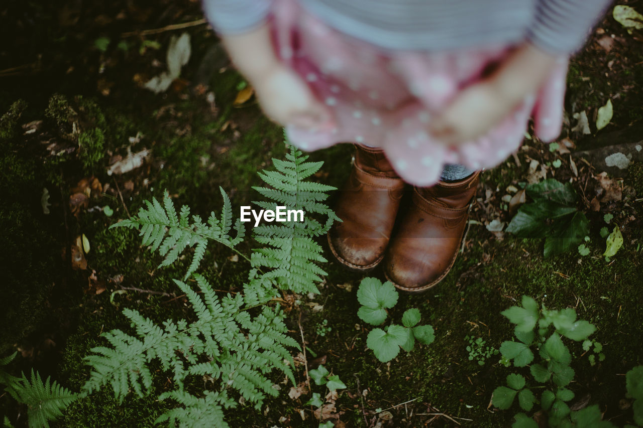 Low section of girls boots standing on ground near plants