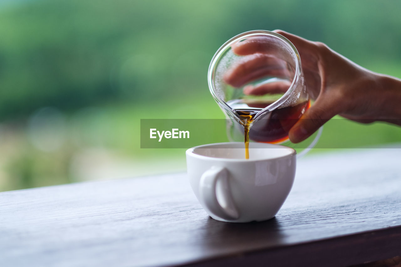 MIDSECTION OF PERSON POURING COFFEE CUP