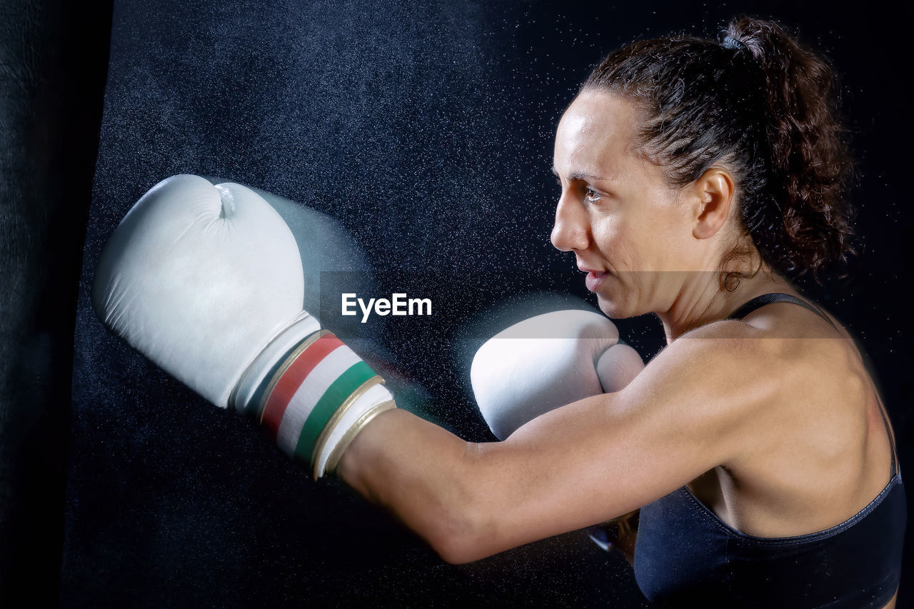 Female boxer punching bag against black background