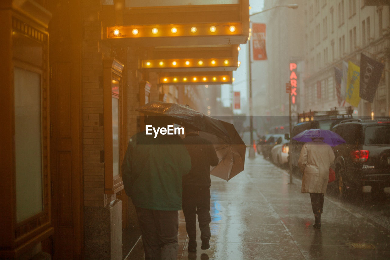 REAR VIEW OF PEOPLE WALKING ON WET ROAD IN RAINY SEASON