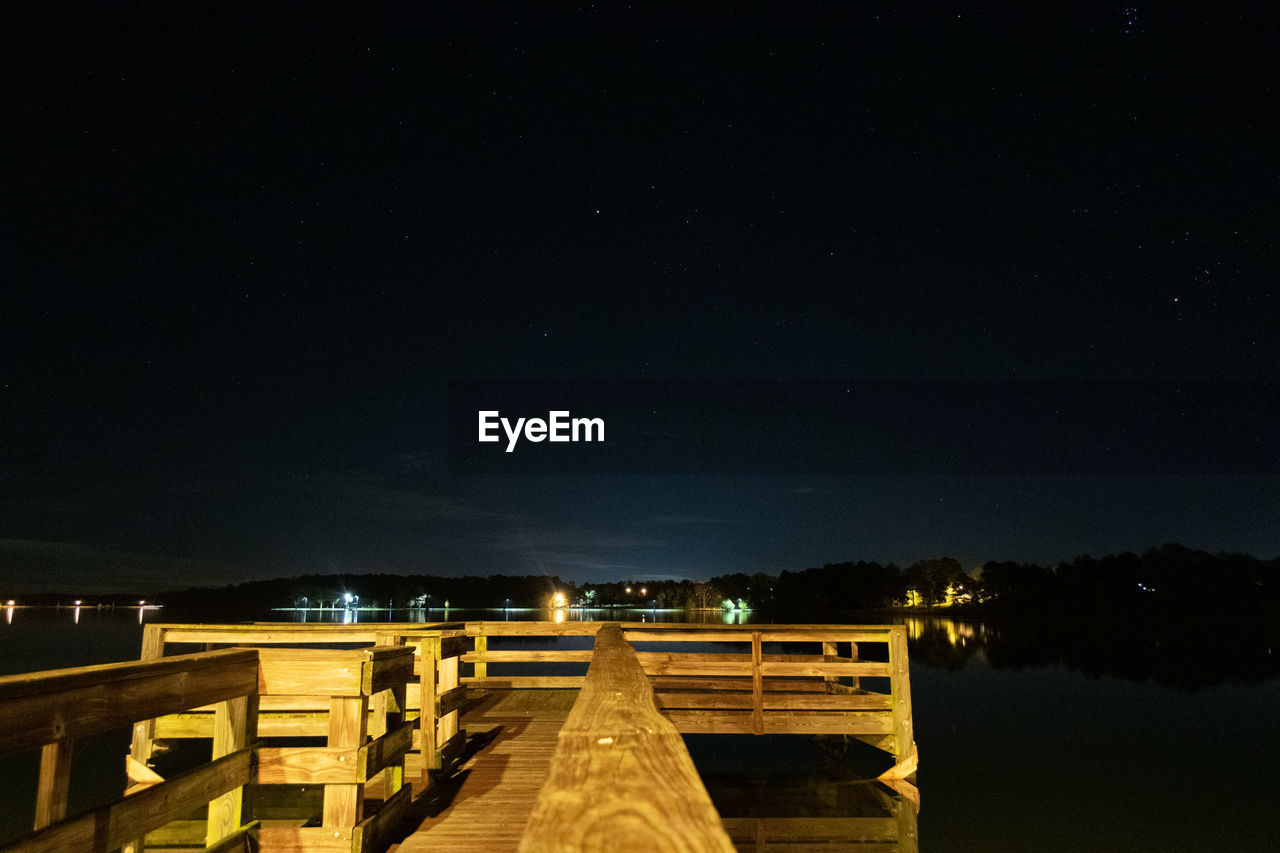 Illuminated pier over lake against sky at night