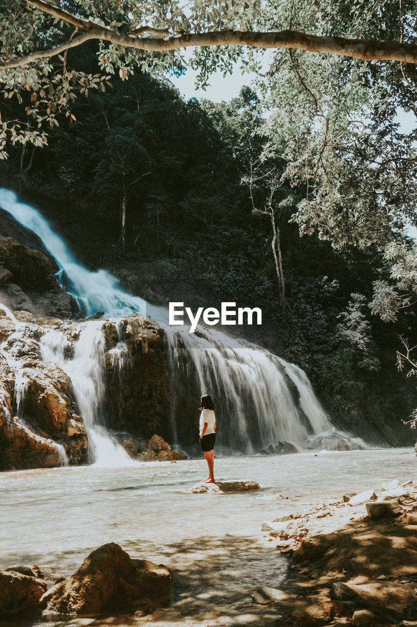 MAN STANDING ON ROCKS AT WATERFALL