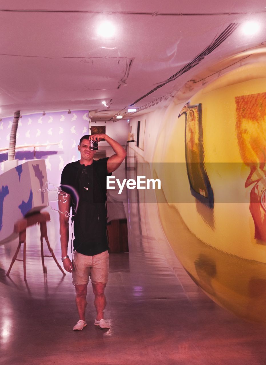 FULL LENGTH REAR VIEW OF MAN PHOTOGRAPHING IN ILLUMINATED BUS