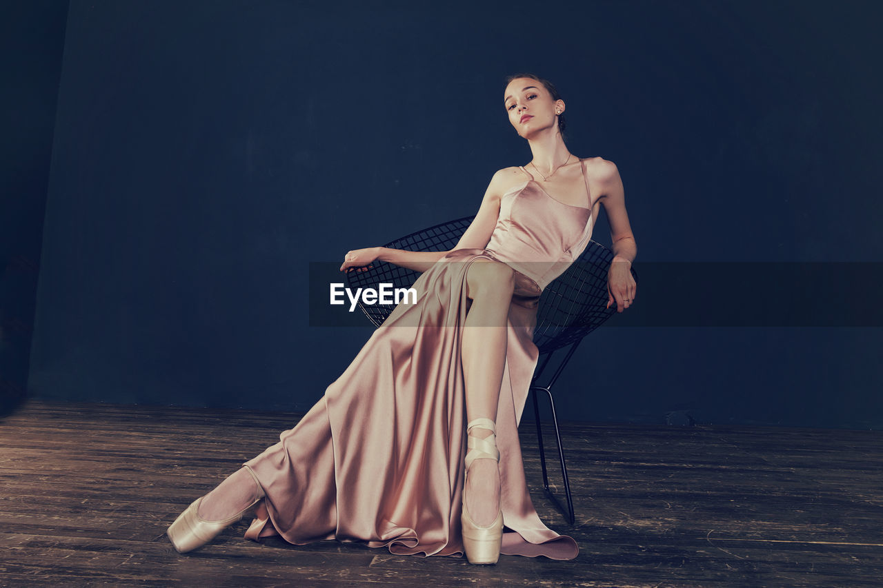 Portrait of a ballerina in a pink dress is sitting on a chair with her leg in the slit of the dress