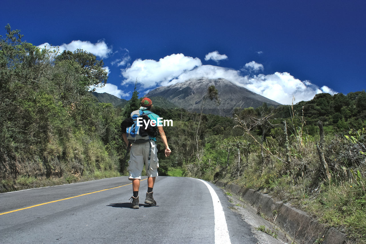 Rear view of hiker walking on road against sky