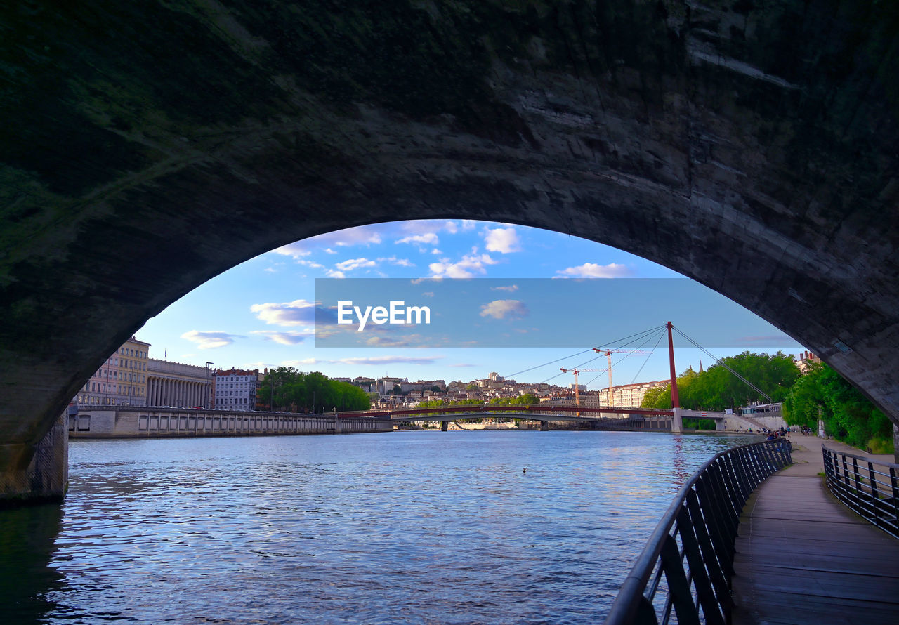 BRIDGE OVER RIVER IN CITY AGAINST SKY SEEN FROM ARCH