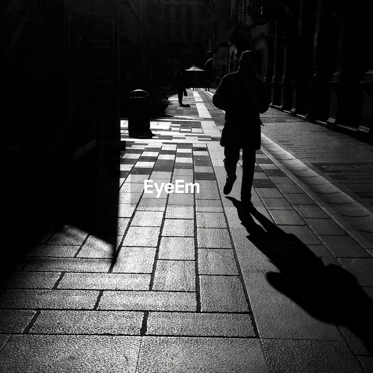 Silhouette of man walking on pavement