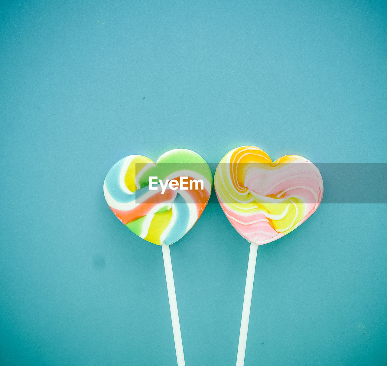 Close-up of colorful heart shape lollipops by turquoise wall