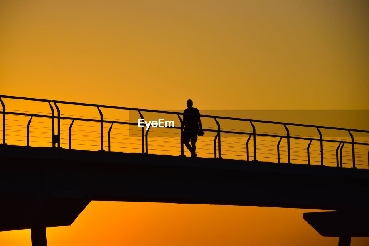 Low angle view of silhouette man on bridge against sky during sunset