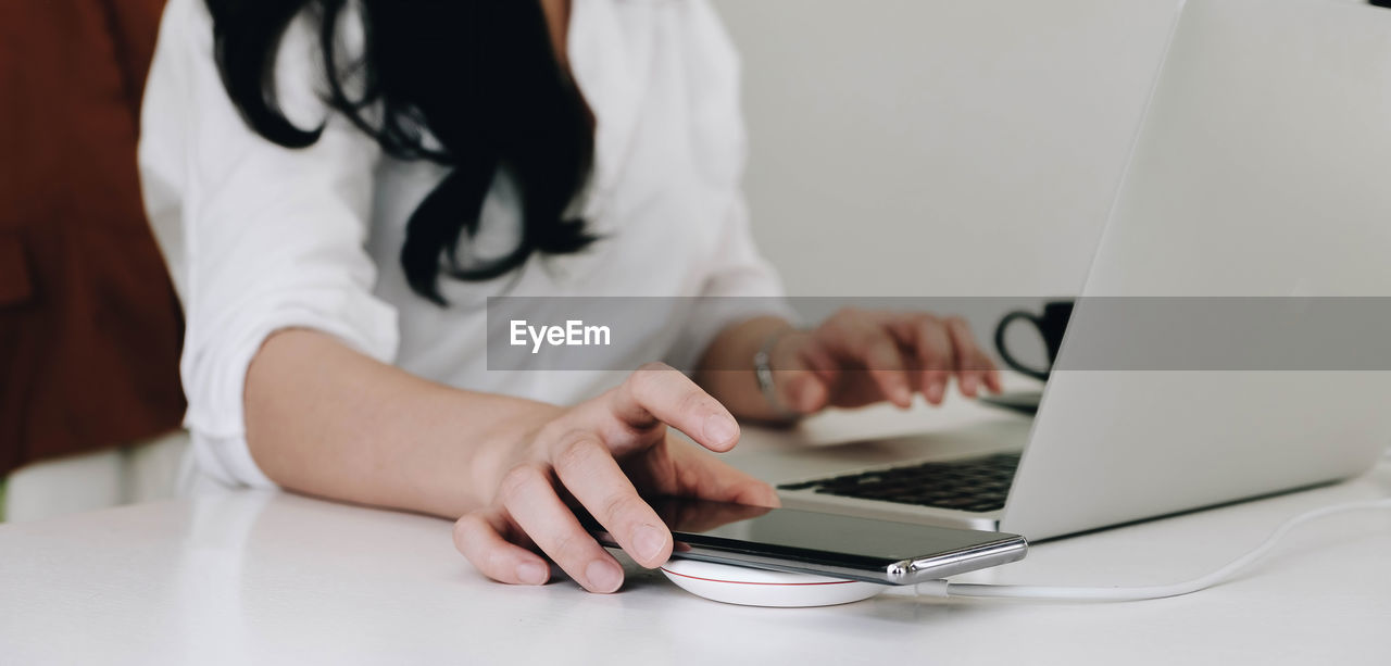 Cropped image of an office woman is charging a smartphone with a wireless charger while typing