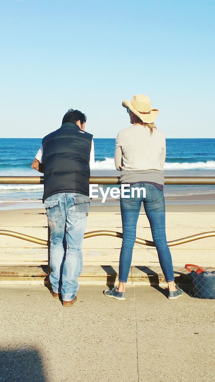 Rear view of man and woman standing on walkway at beach 