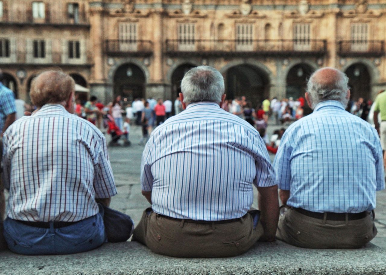 Rear view of men sitting in front of old building in city