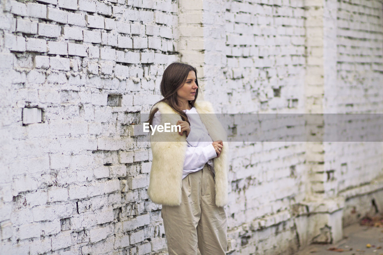 Full length of a smiling young woman standing against wall